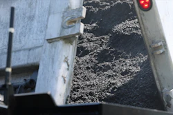 Truck bed filled with dark crushed stone aggregate material with red traffic light visible