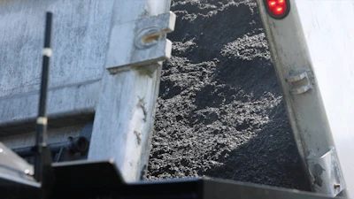 Truck bed filled with dark crushed stone aggregate material with red traffic light visible