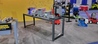 Trade show exhibition floor displaying industrial equipment, machinery, and blue signage with yellow wall backdrop