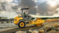 Yellow Volvo road roller compacting gravel at construction site under cloudy sky