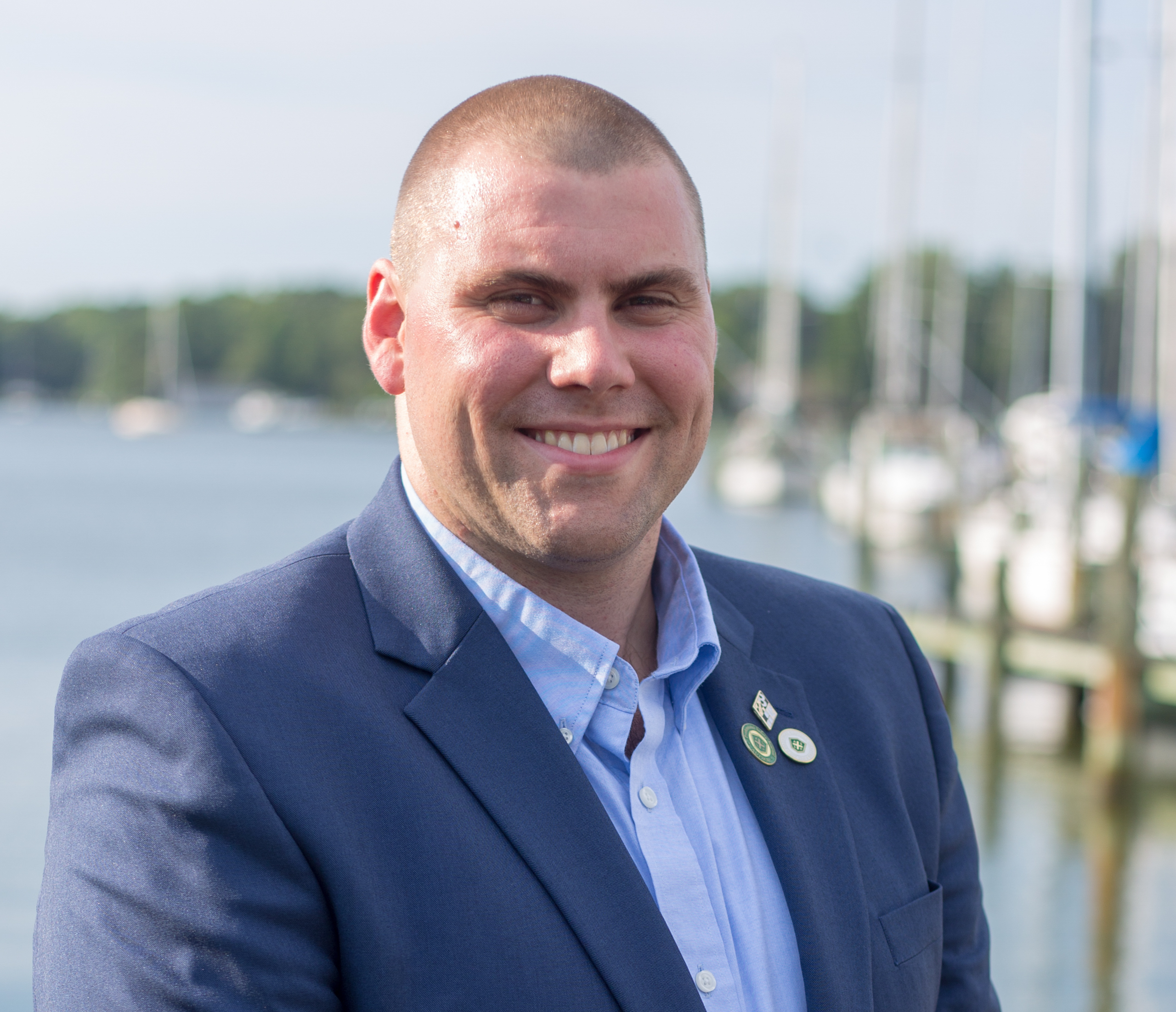 Professional man in navy blazer smiling at marina with sailboats in background Headshot
