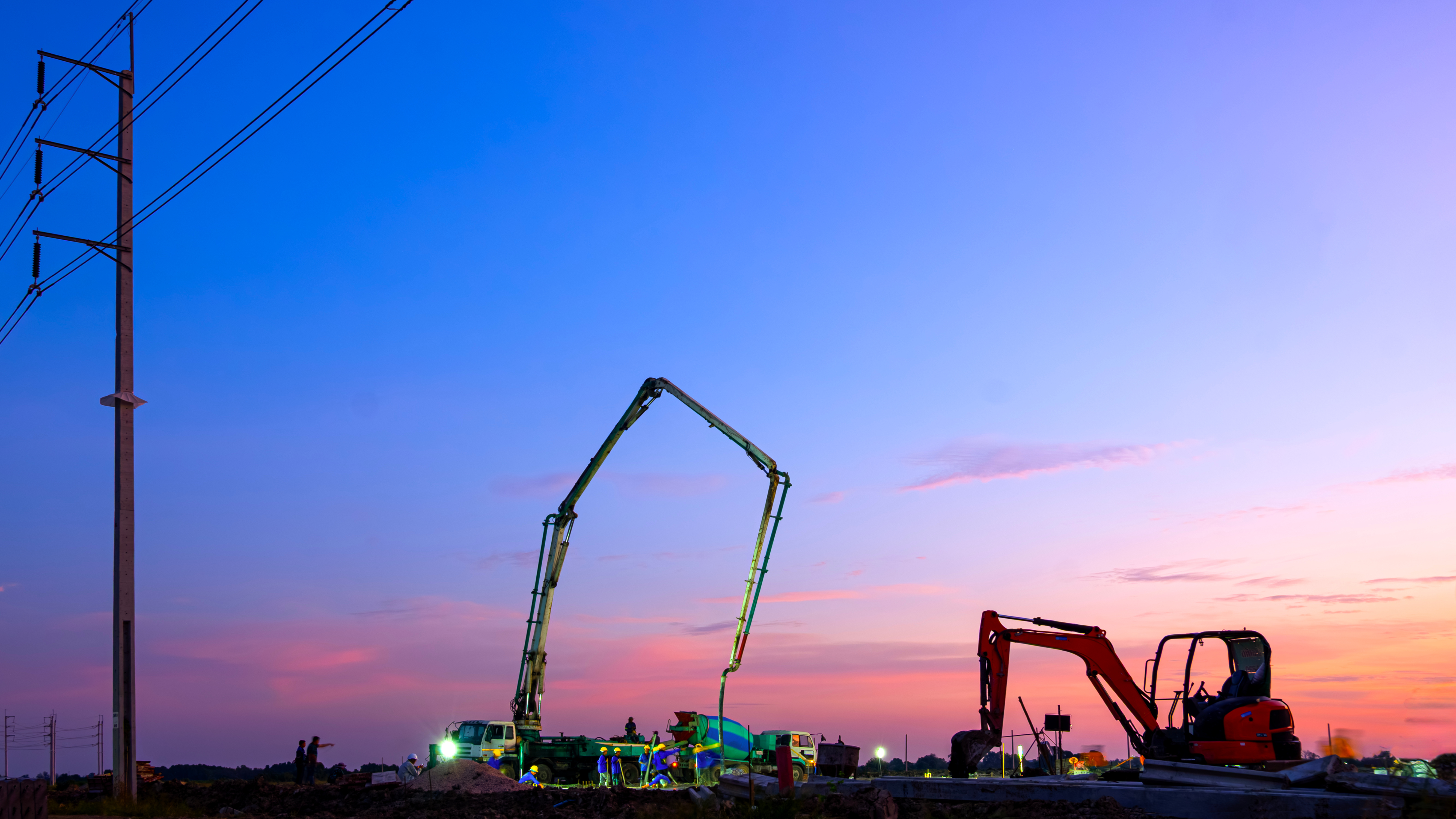 Construction equipment silhouetted against twilight sky with power lines and colorful sunset clouds