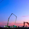 Construction equipment silhouetted against twilight sky with power lines and colorful sunset clouds