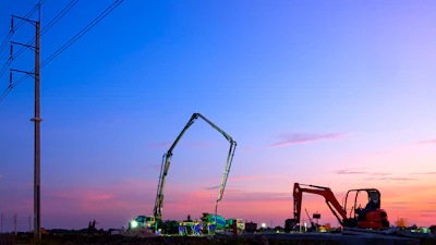 Construction equipment silhouetted against twilight sky with power lines and colorful sunset clouds