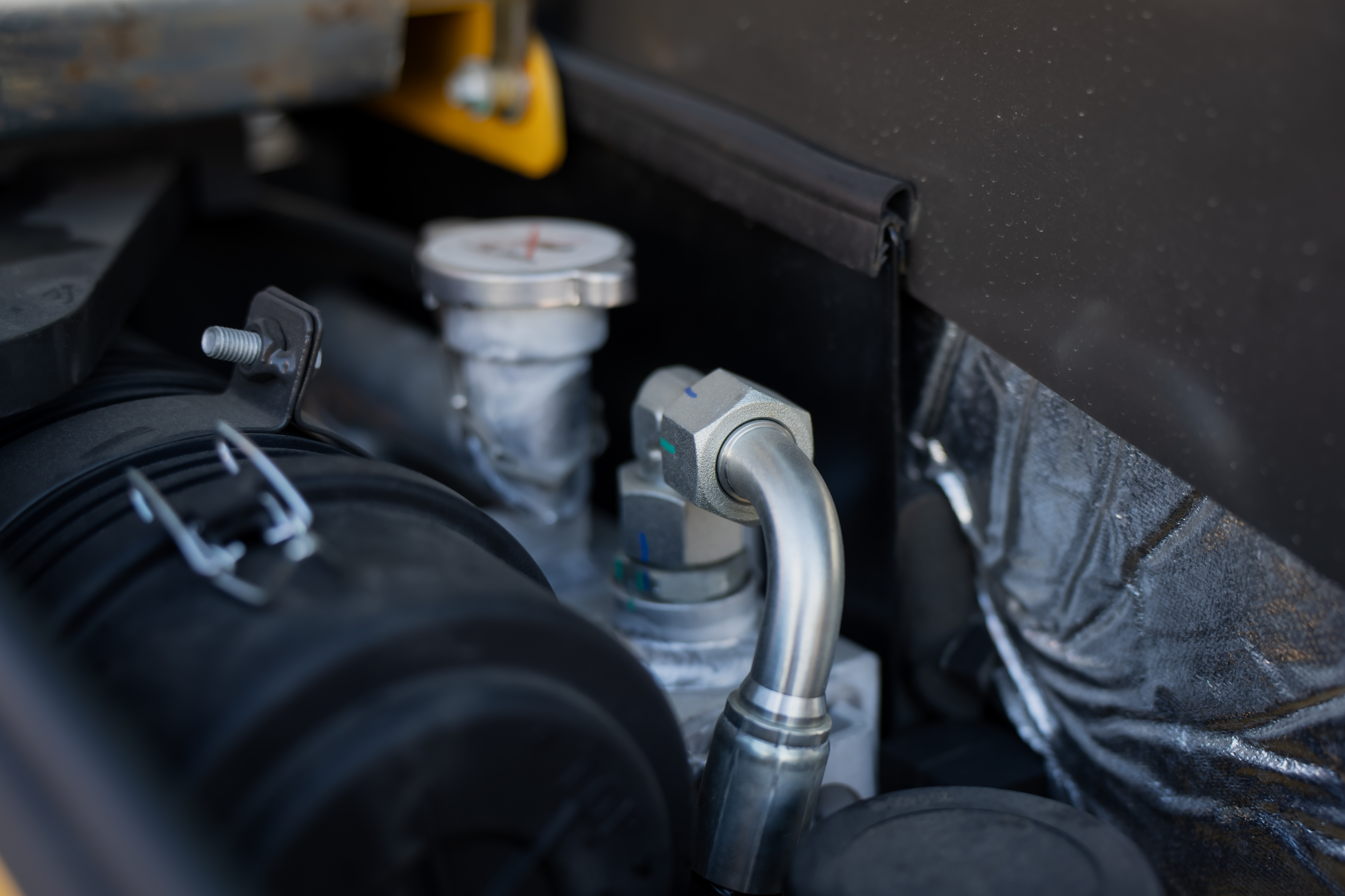 Close-up of engine bay components including hoses, connectors, and fluid reservoirs in a vehicle engine compartment