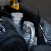 Close-up of engine bay components including hoses, connectors, and fluid reservoirs in a vehicle engine compartment