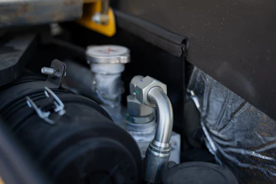 Close-up of engine bay components including hoses, connectors, and fluid reservoirs in a vehicle engine compartment