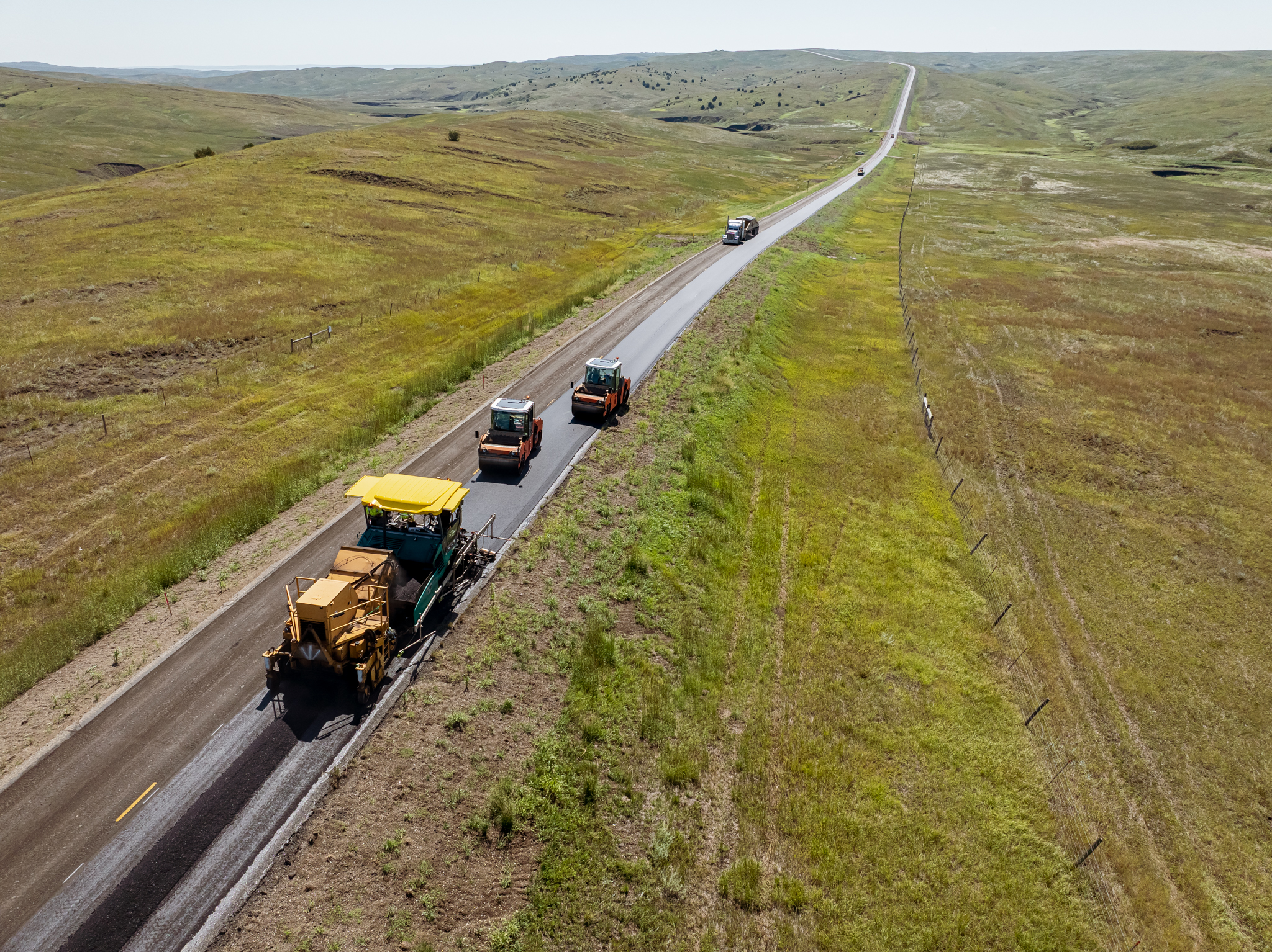 Aerial view of highway with construction vehicles and equipment traveling through rolling grassland hills