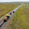 Aerial view of highway with construction vehicles and equipment traveling through rolling grassland hills