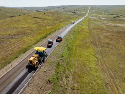 Aerial view of highway with construction vehicles and equipment traveling through rolling grassland hills