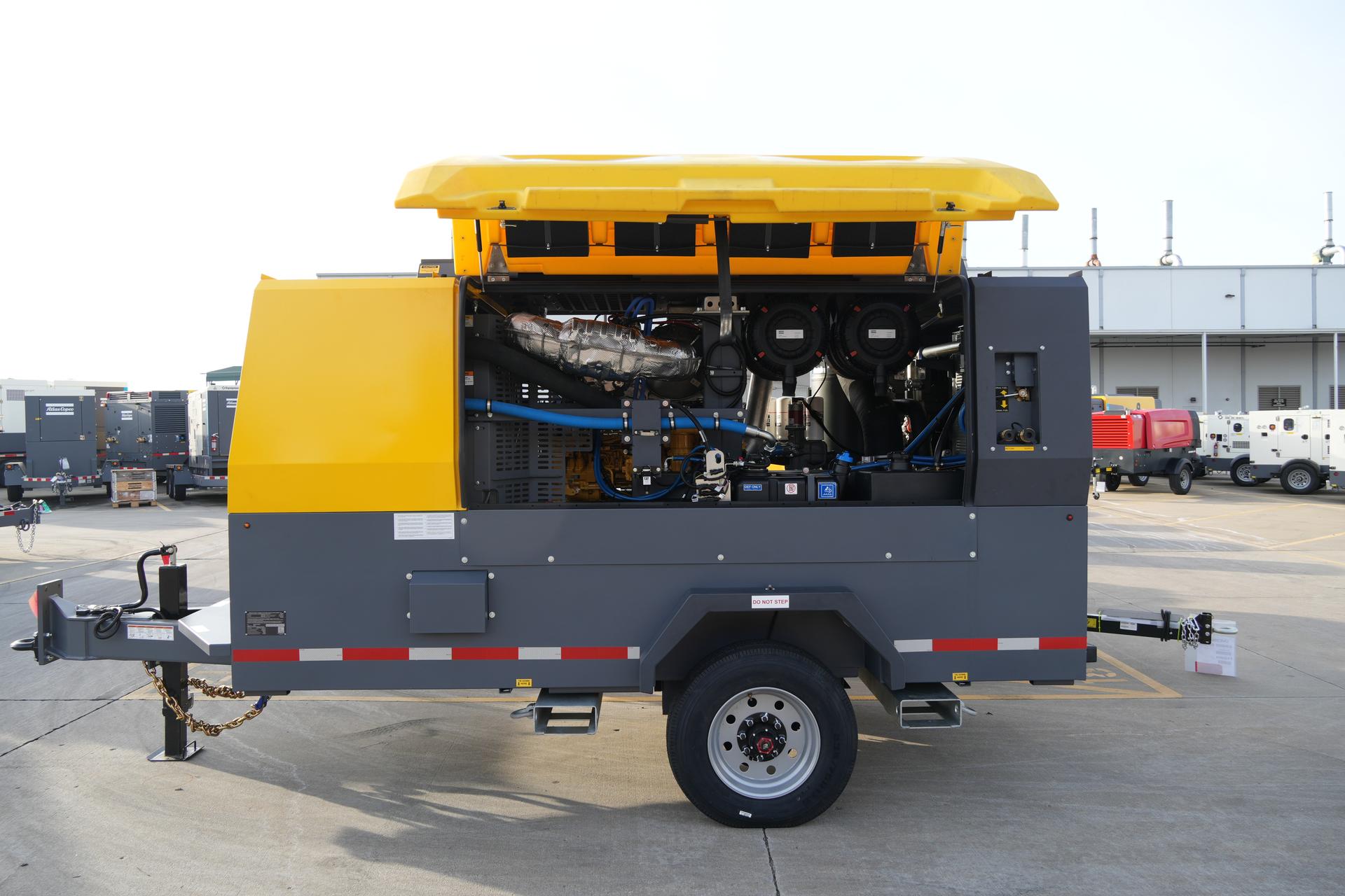Yellow and gray mobile power generator trailer with engine compartment open in industrial yard