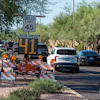 Speed monitoring sign displaying vehicle speeds on a residential street with construction barriers and parked cars