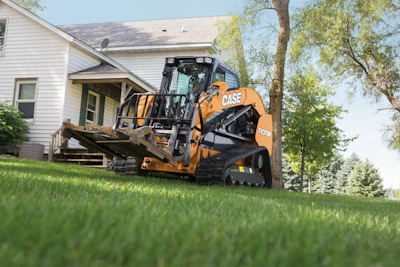 Orange and black CASE skid steer loader positioned on grass beside a white residential house with trees