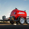 Red CRAFCO tanker trailer with dual axles parked in industrial yard under clear sky