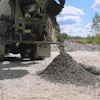 Concrete mixer truck discharging aggregate at construction site with stockpiles and trees