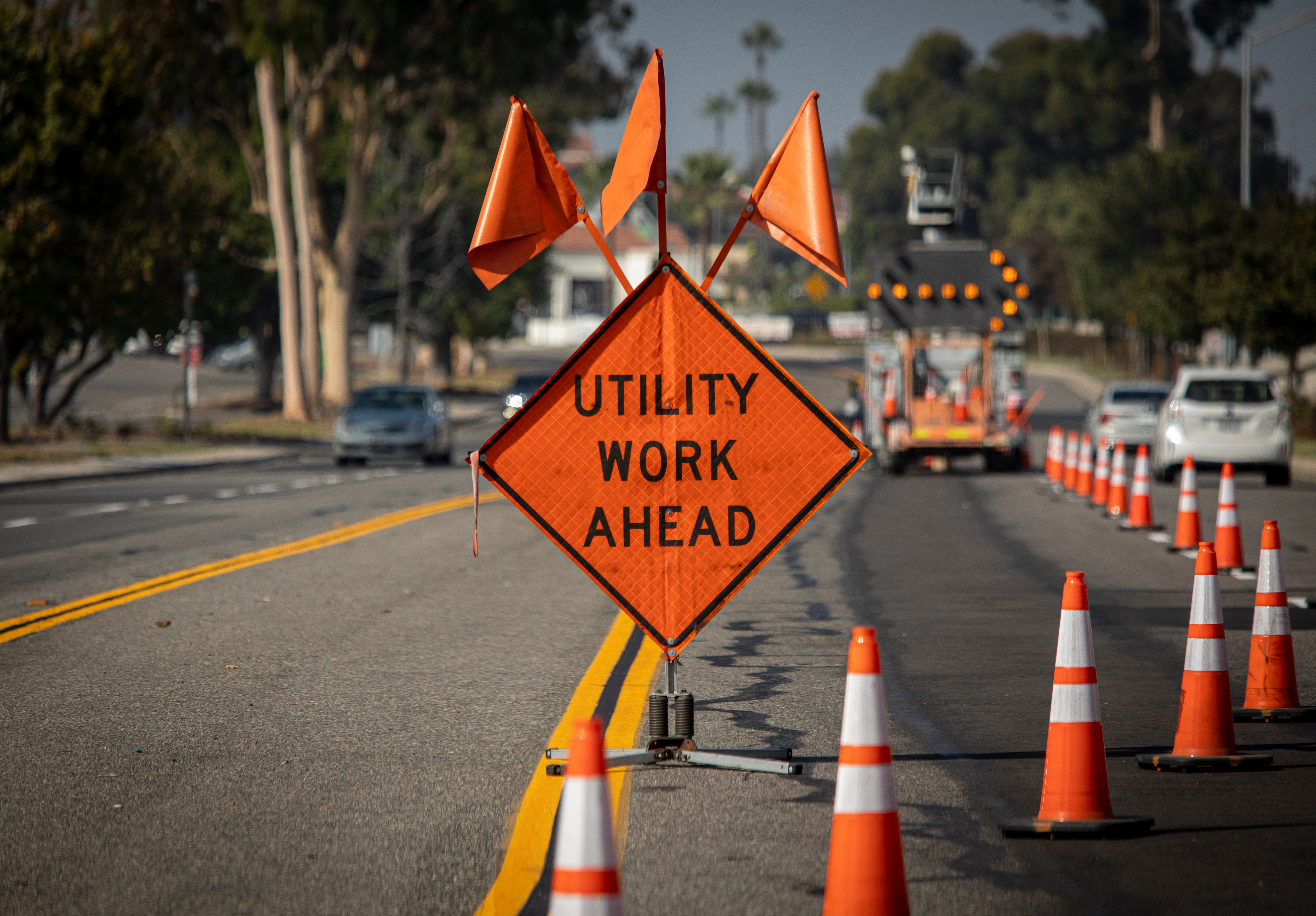 Orange diamond-shaped construction warning sign reading 'UTILITY WORK AHEAD' on a street with traffic cones and equipment