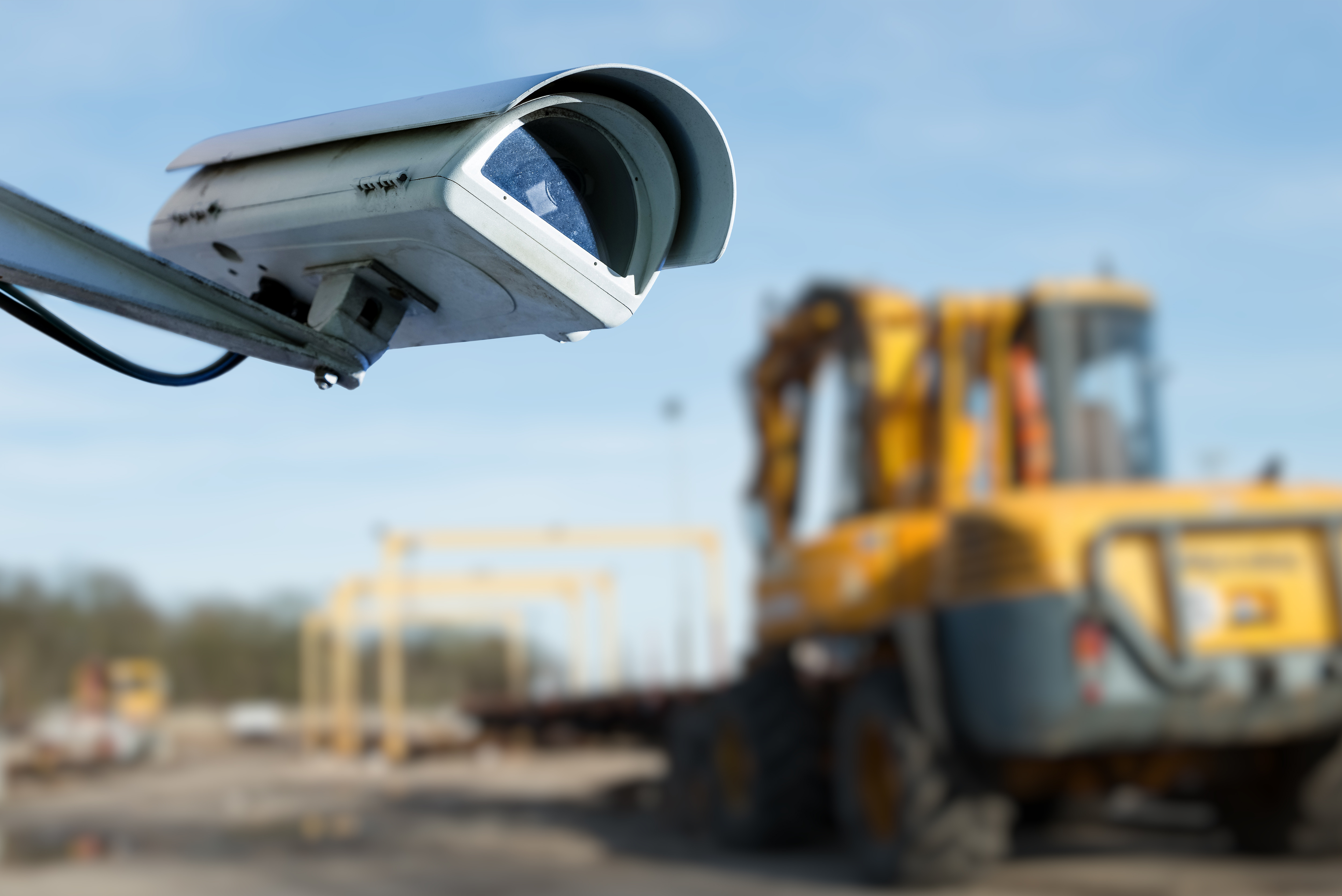 Security camera mounted on pole overlooking construction site with yellow excavator and steel framework