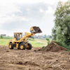Yellow wheel loader scooping soil at construction site with rural landscape and trees in background