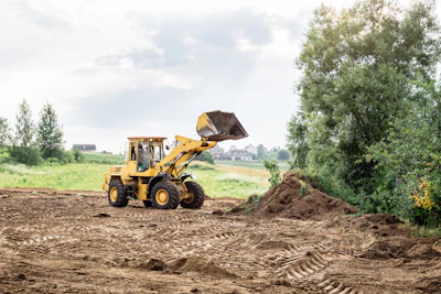 Yellow wheel loader scooping soil at construction site with rural landscape and trees in background