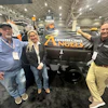 Three professionals pose with Construction Angels branded equipment at an indoor trade show or exhibition