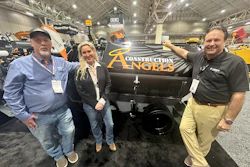Three professionals pose with Construction Angels branded equipment at an indoor trade show or exhibition