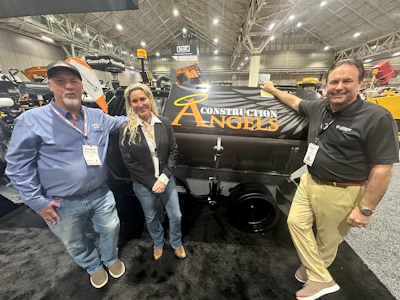 Three professionals pose with Construction Angels branded equipment at an indoor trade show or exhibition