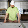Construction worker in safety gear reviewing building blueprints at a workbench in a garage.
