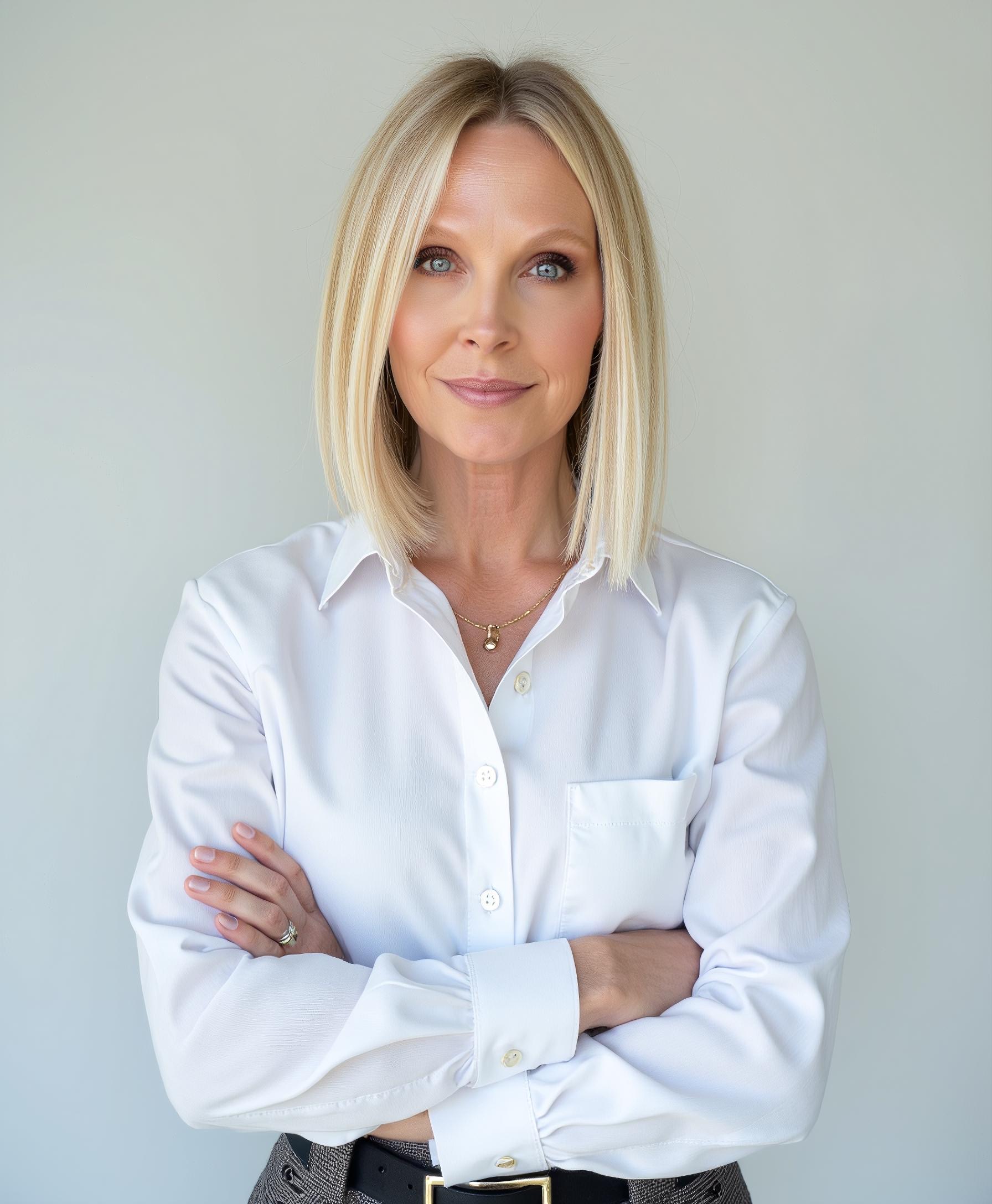 Professional woman in white button-up shirt with arms crossed, smiling at camera against neutral background Headshot