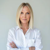 Professional woman in white button-up shirt with arms crossed, smiling at camera against neutral background