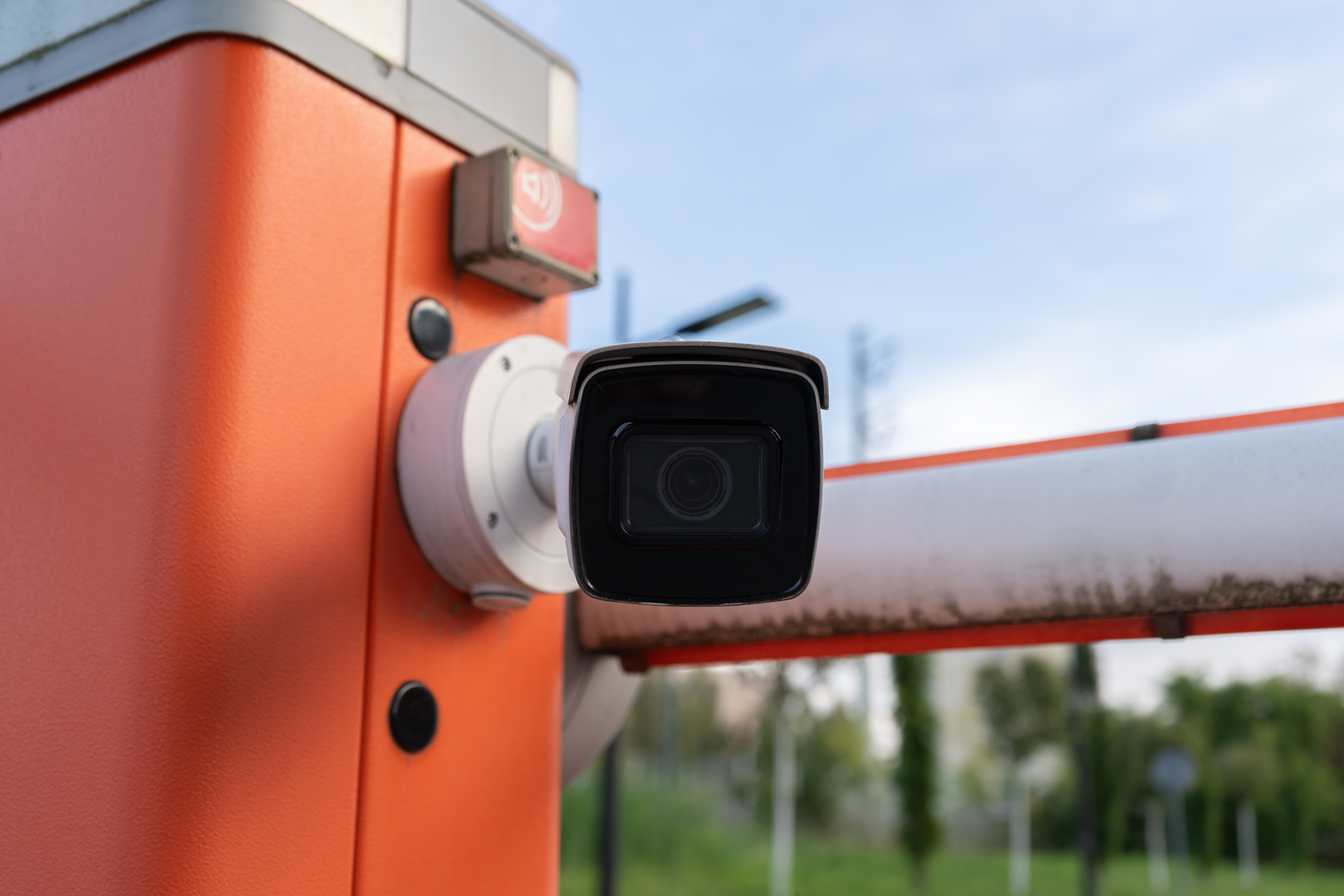 Security camera mounted on orange pole with orange cable in outdoor industrial setting