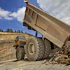 Dump truck unloading rocks and gravel at quarry with blue sky and trees in background