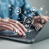 Hands typing on laptop with digital security and cloud computing icons floating above in connected network pattern