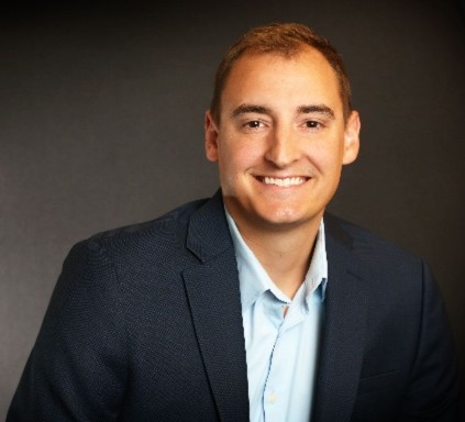 Professional headshot of a smiling man in business attire wearing a navy blazer and light blue shirt Headshot
