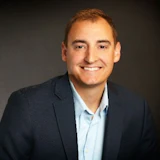 Professional headshot of a smiling man in business attire wearing a navy blazer and light blue shirt