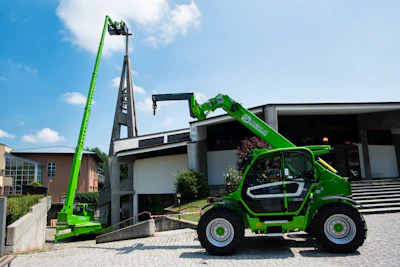 Bright green Merlo telehandler with extended boom positioned outside modern industrial building