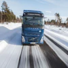 Blue Volvo hydrogen-powered truck driving on snowy road through forested landscape