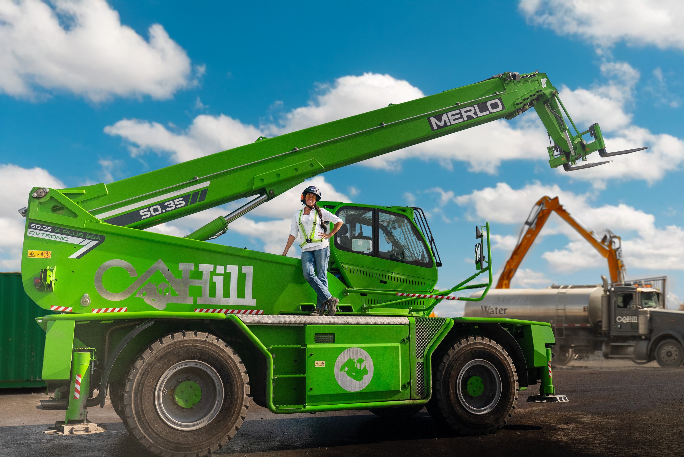 Green Merlo telescopic handler with operator on construction site under blue sky