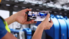Person holding smartphone recording video inside industrial facility with blue equipment