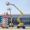 Construction equipment display yard featuring various aerial lifts and scissor lifts in red and yellow against industrial buildings.