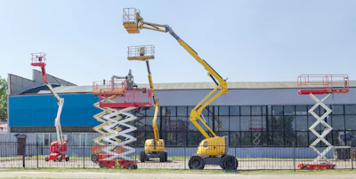 Construction equipment display yard featuring various aerial lifts and scissor lifts in red and yellow against industrial buildings.