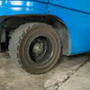 Worn tire and wheel of a blue bus parked on concrete ground
