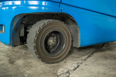 Worn tire and wheel of a blue bus parked on concrete ground