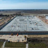 Aerial view of large industrial construction site with concrete foundation and electrical infrastructure surrounded by farmland