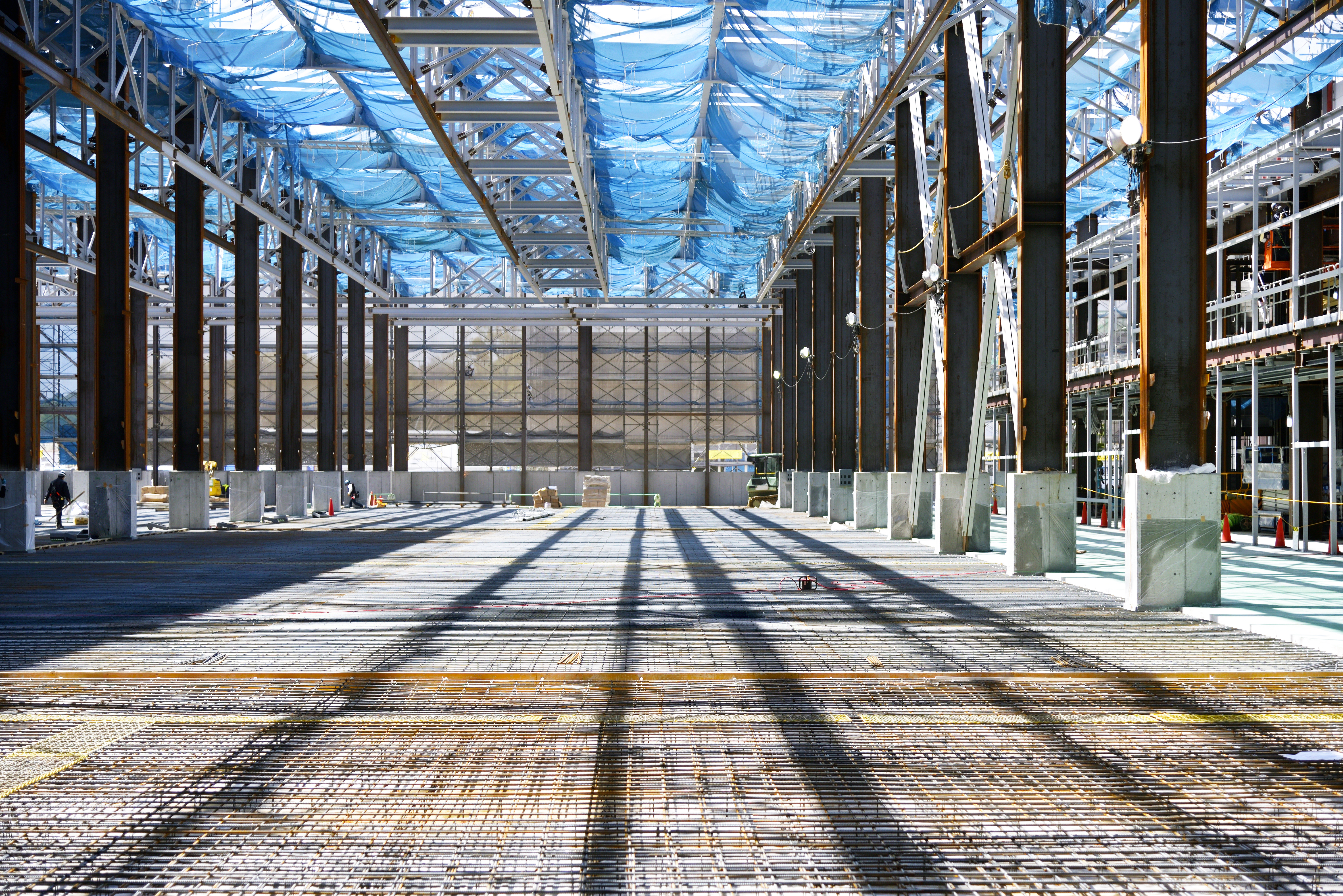Interior of large industrial greenhouse with metal framework, blue plastic roof panels, concrete pillars, and paved flooring