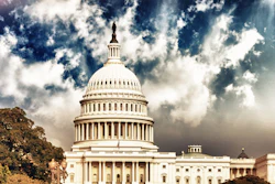 U.S. Capitol Building dome against dramatic cloudy sky with golden sunlight and surrounding trees