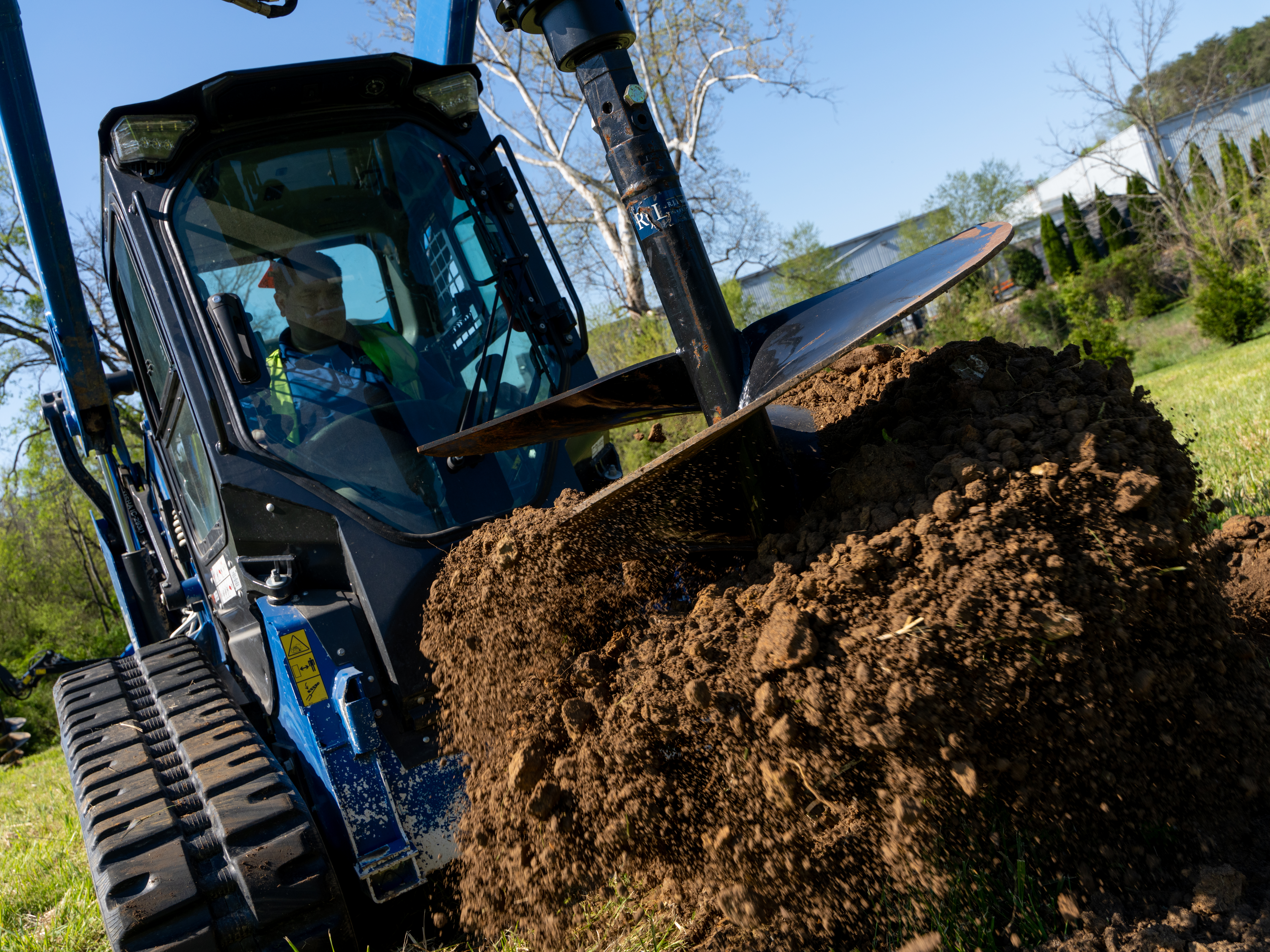 Blue skid steer loader moving pile of dark soil during landscaping work on hillside