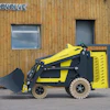 Yellow and black ECOVOLVE compact loader with bucket attachment positioned against wooden building