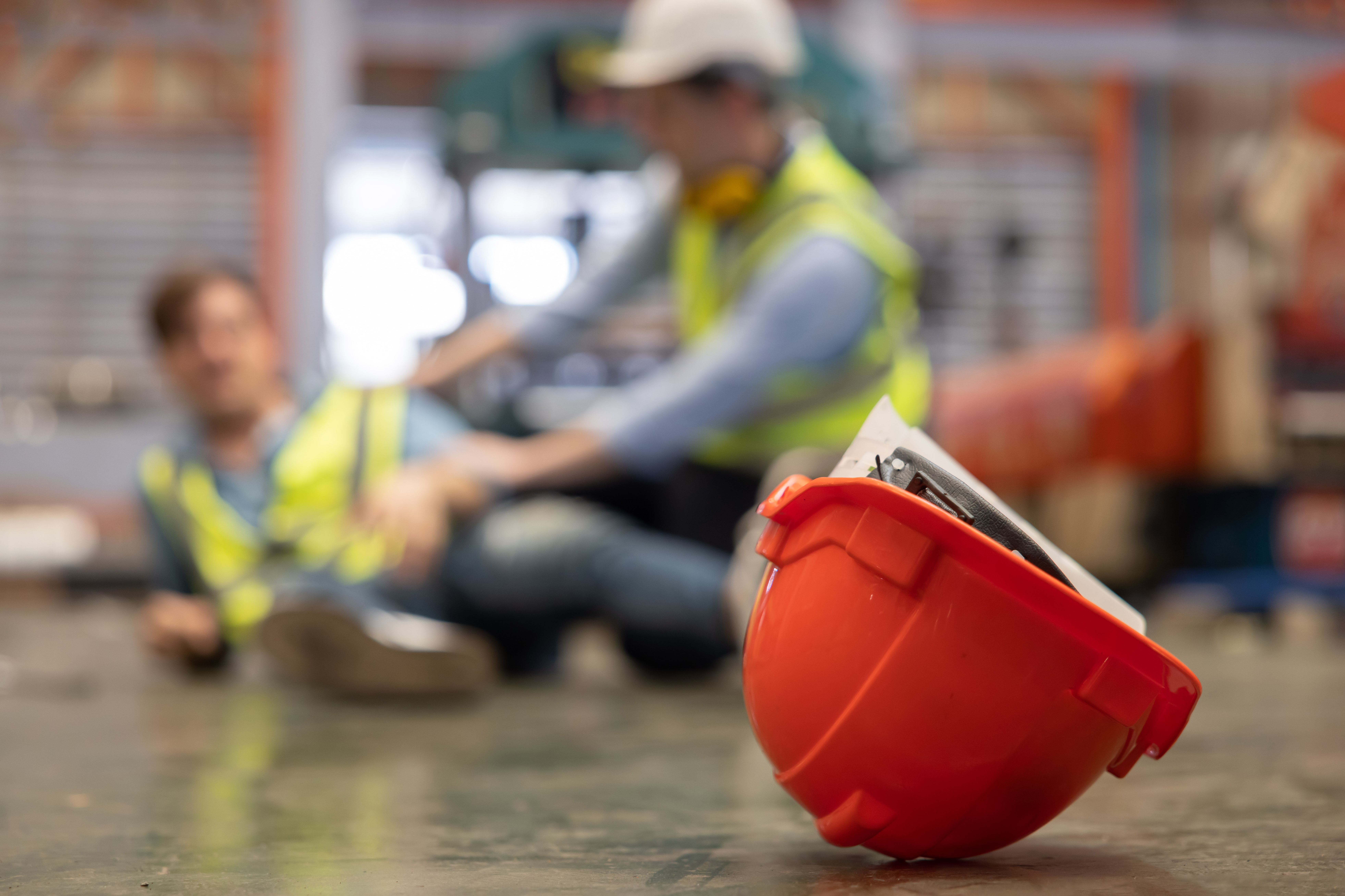 Red hard hat in foreground with construction workers in safety vests on industrial site