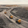 Heavy dump trucks navigate winding roads through an active quarry or mining site with excavated terrain and stockpiled materials.