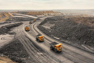 Heavy dump trucks navigate winding roads through an active quarry or mining site with excavated terrain and stockpiled materials.